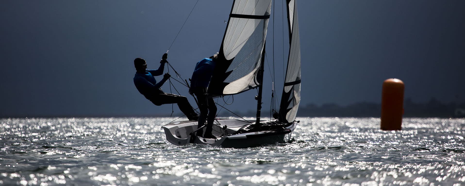 RS500 silhouetted against sunlit water with the crew on trapeze