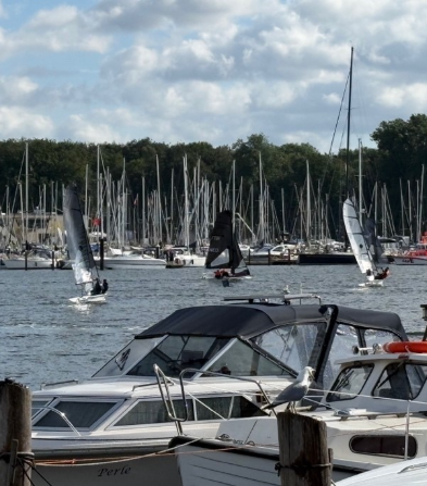 Sailboats and a motorboat docked at a marina with sail-rigged vessels in the background.